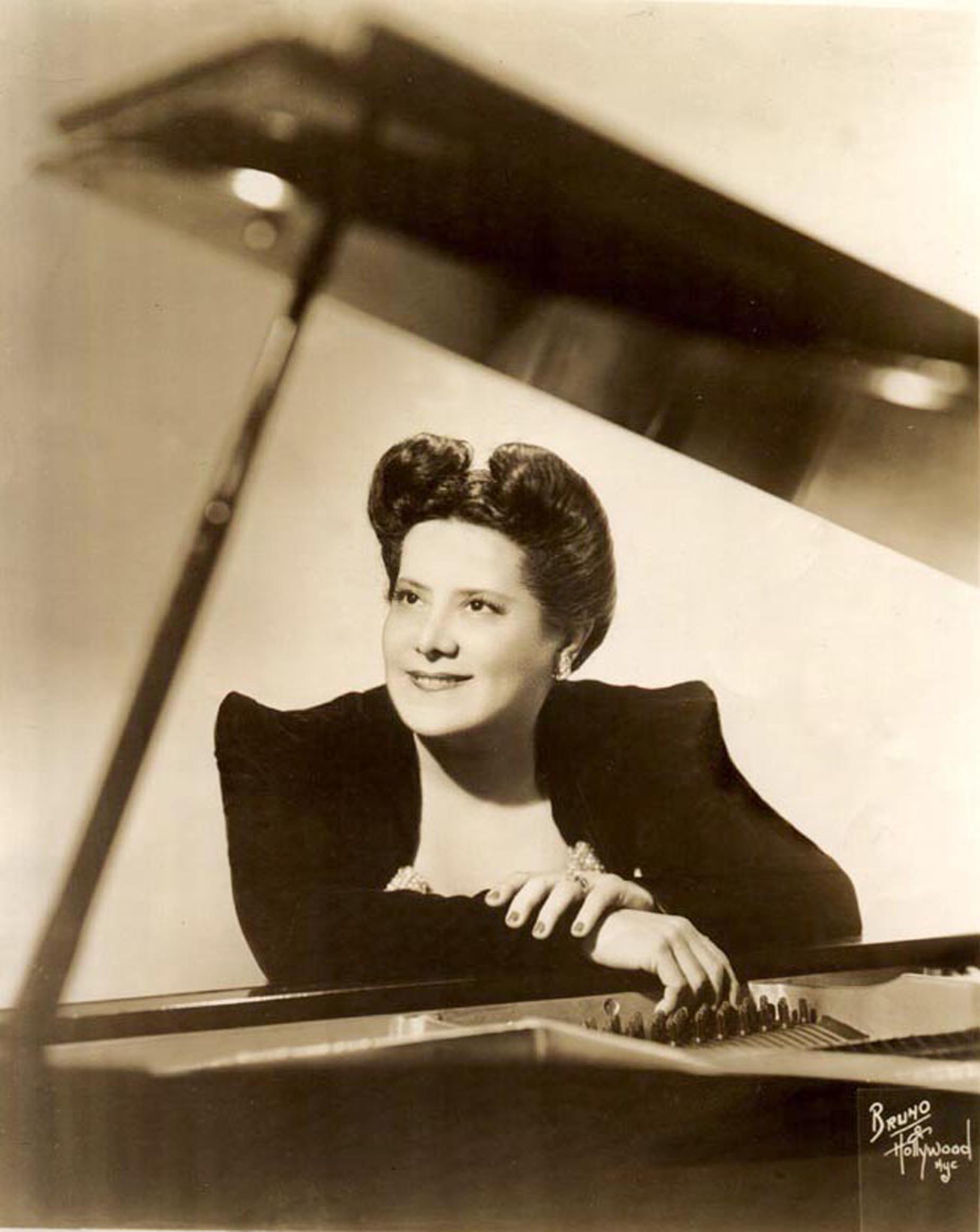 Retrato de estúdio de Guiomar Novaes apoiada ao piano de cauda